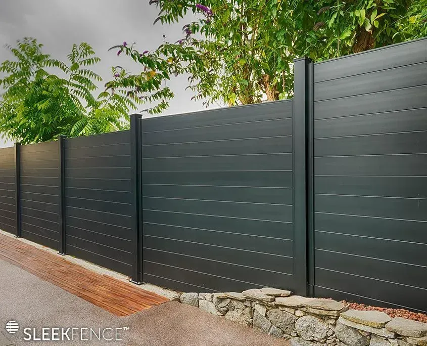 Dark gray horizontal slat fence with black posts, bordering a walkway and greenery.