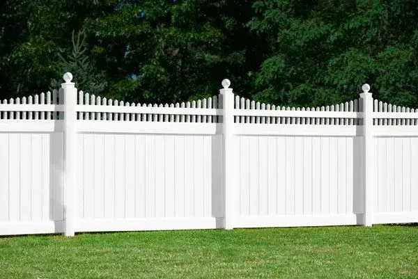 White picket fence in front of green grass and trees.