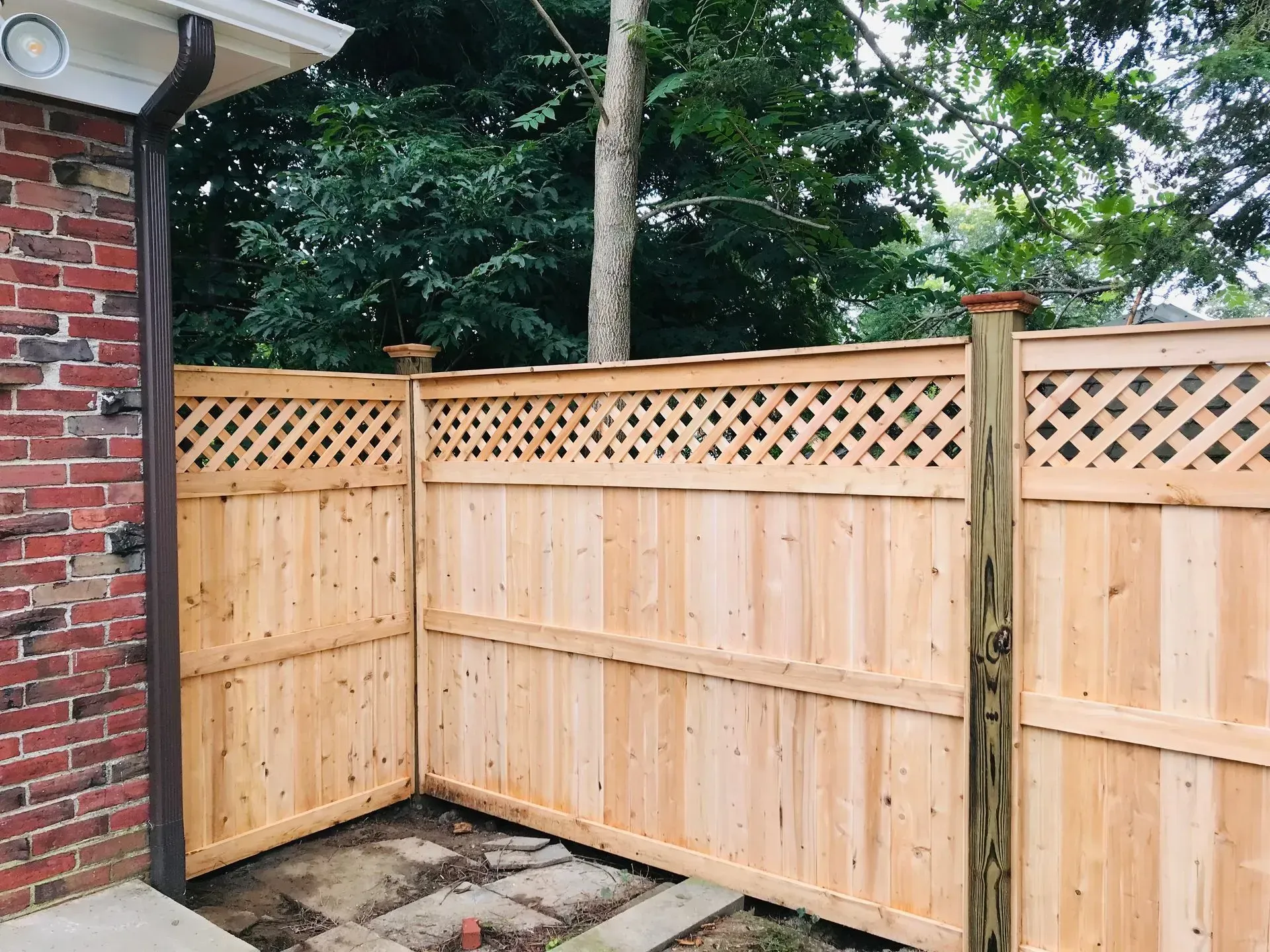 Wooden privacy fence with lattice detail, adjacent to brick wall and trees.
