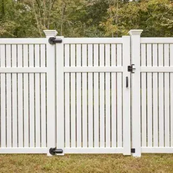 White vinyl fence with gate, set in a grassy area with trees in the background.